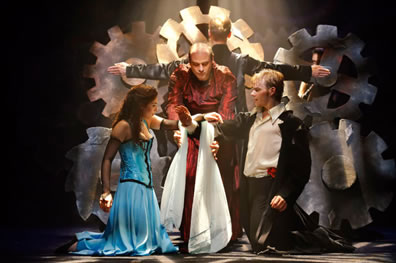 Friar Laurence wraps a white scarf around Juliet's and Romeo's hands, with gears in the background and another dancer posed as the cross in the church